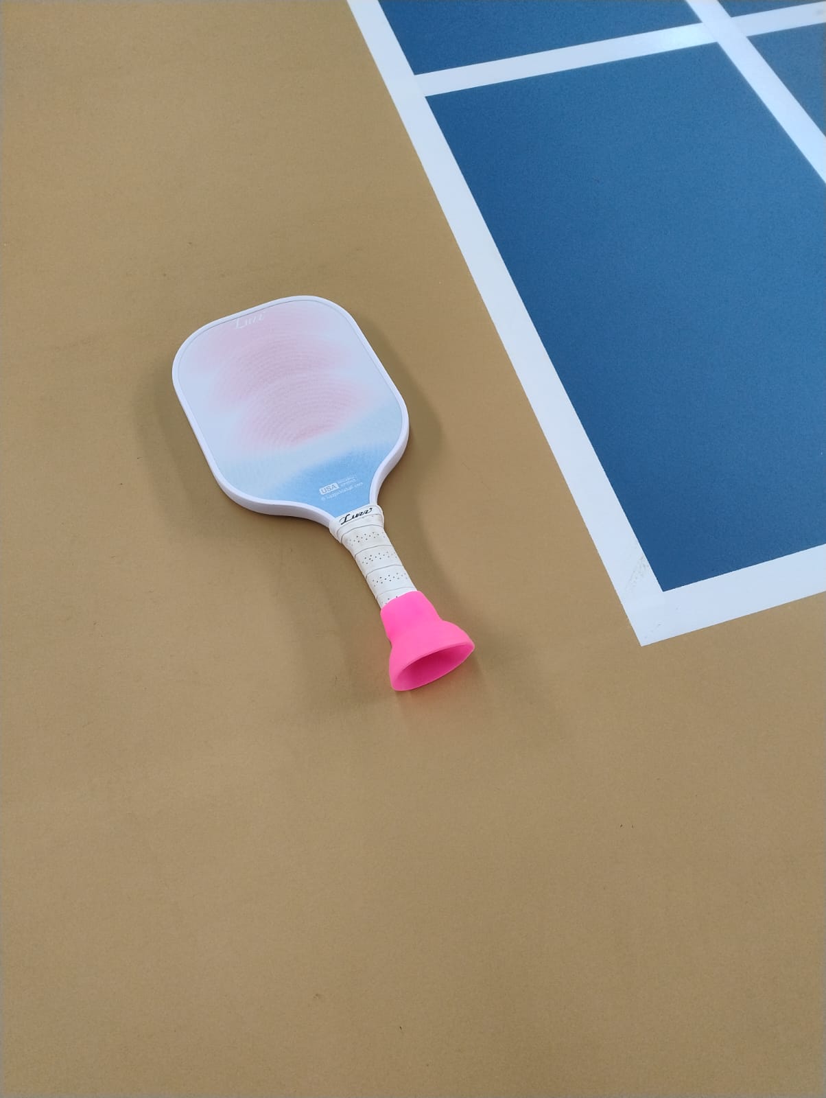 A pink suction-cup ball pickup attachment fitted to the end of a pickleball paddle handle